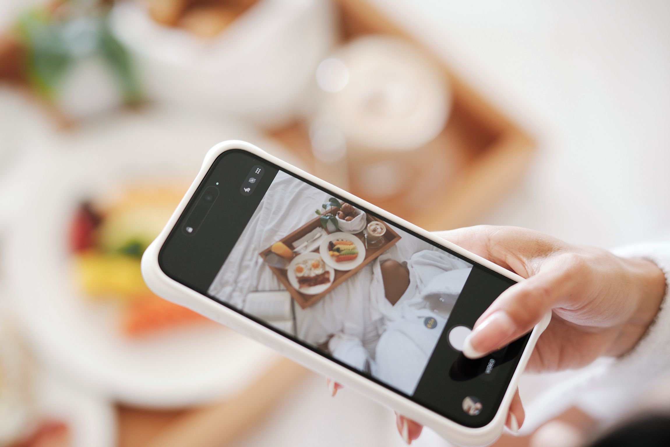 A hand holding a smartphone displaying a photo of a breakfast tray with various foods.