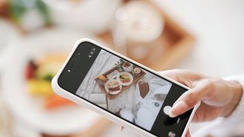 A hand holding a smartphone displaying a photo of a breakfast tray with various foods.