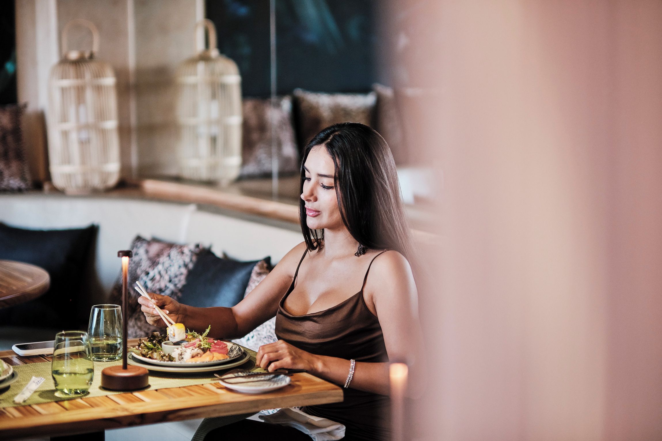 A person dining at a table with a plate of food, chopsticks, and glasses of water.