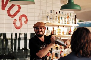 Un cantinero preparando una bebida detrás de la barra, con estantes llenos de botellas.