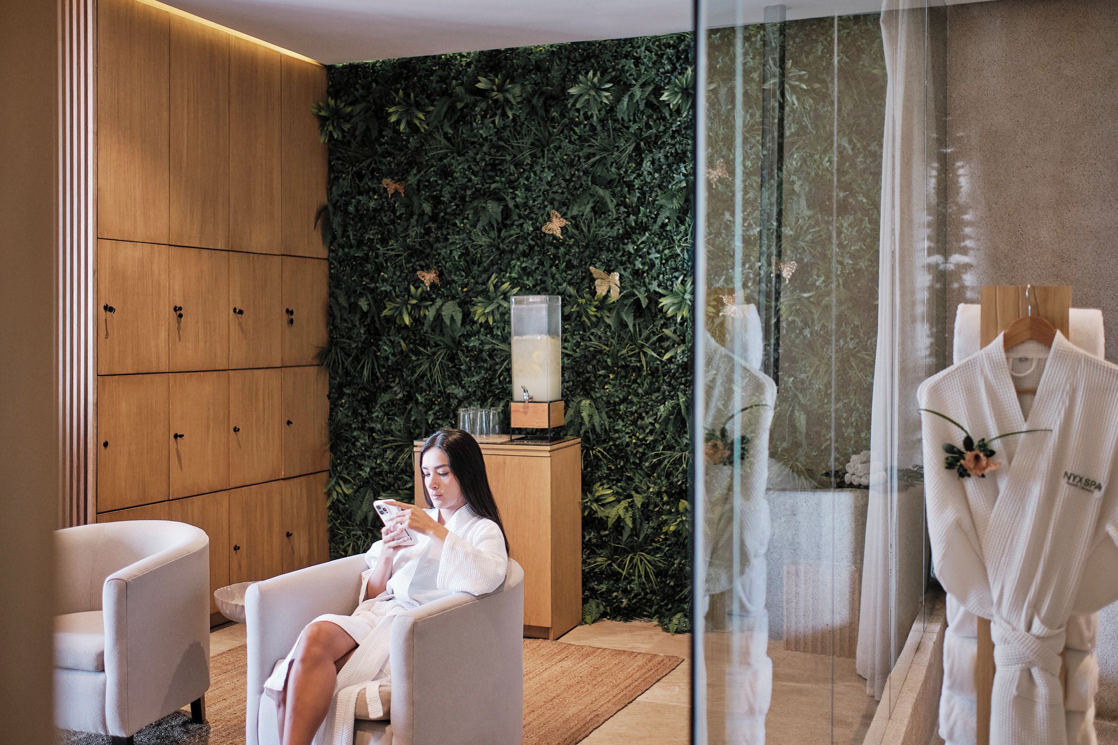 A spa room with a wooden cabinet, a glass partition, and a plant wall.