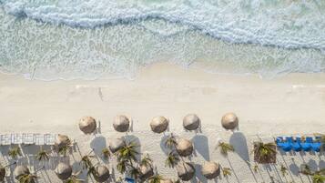 Une plage avec des vagues, des parasols et des palmiers.