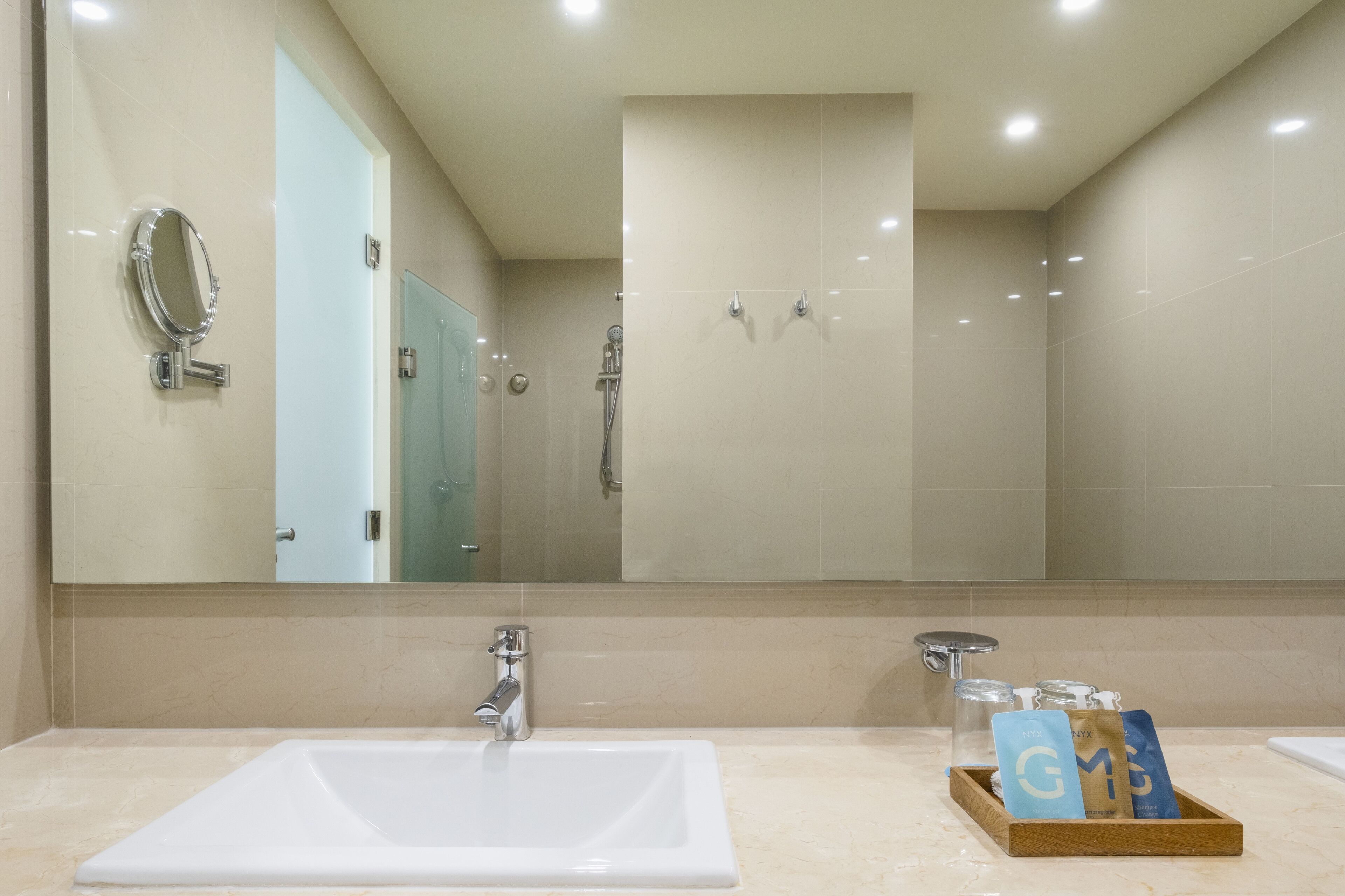 Bagno con un ampio specchio, un lavandino e una cabina doccia. Prodotti da bagno in un vassoio sul ripiano.