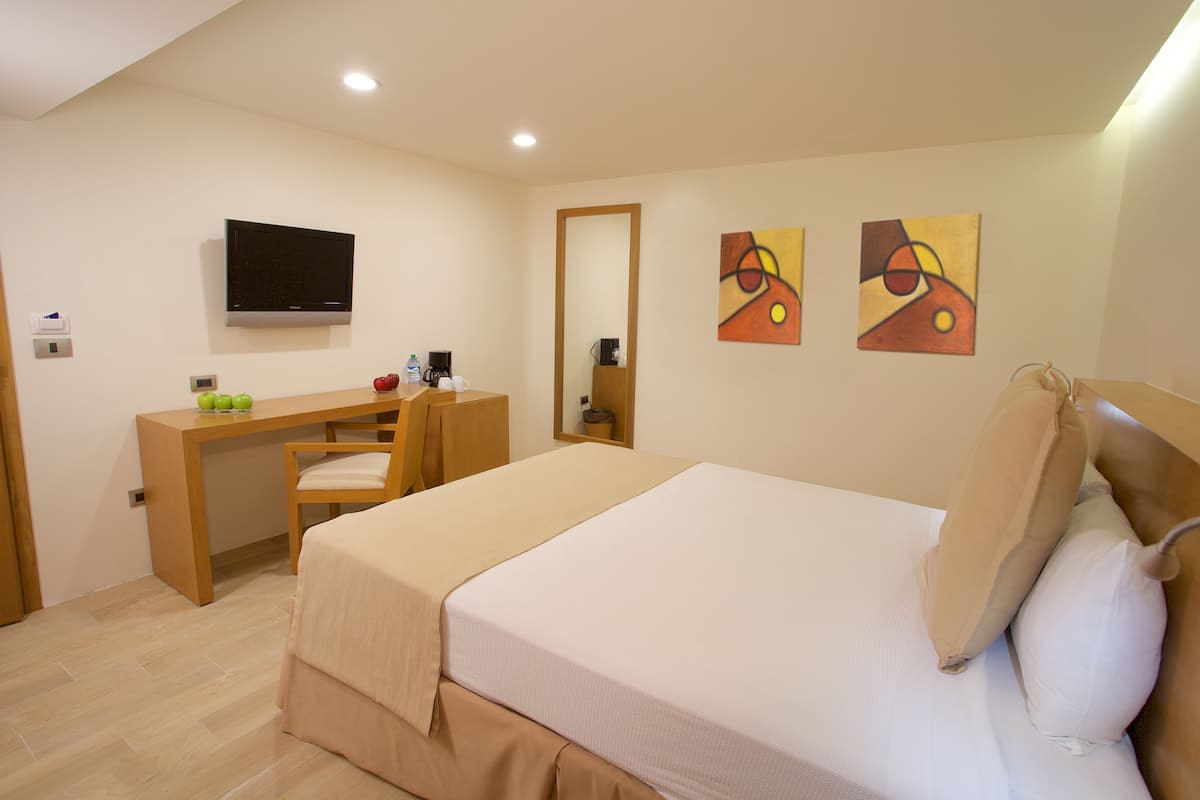 Habitación de hotel con cama, escritorio, silla, televisor y obras de arte en las paredes.