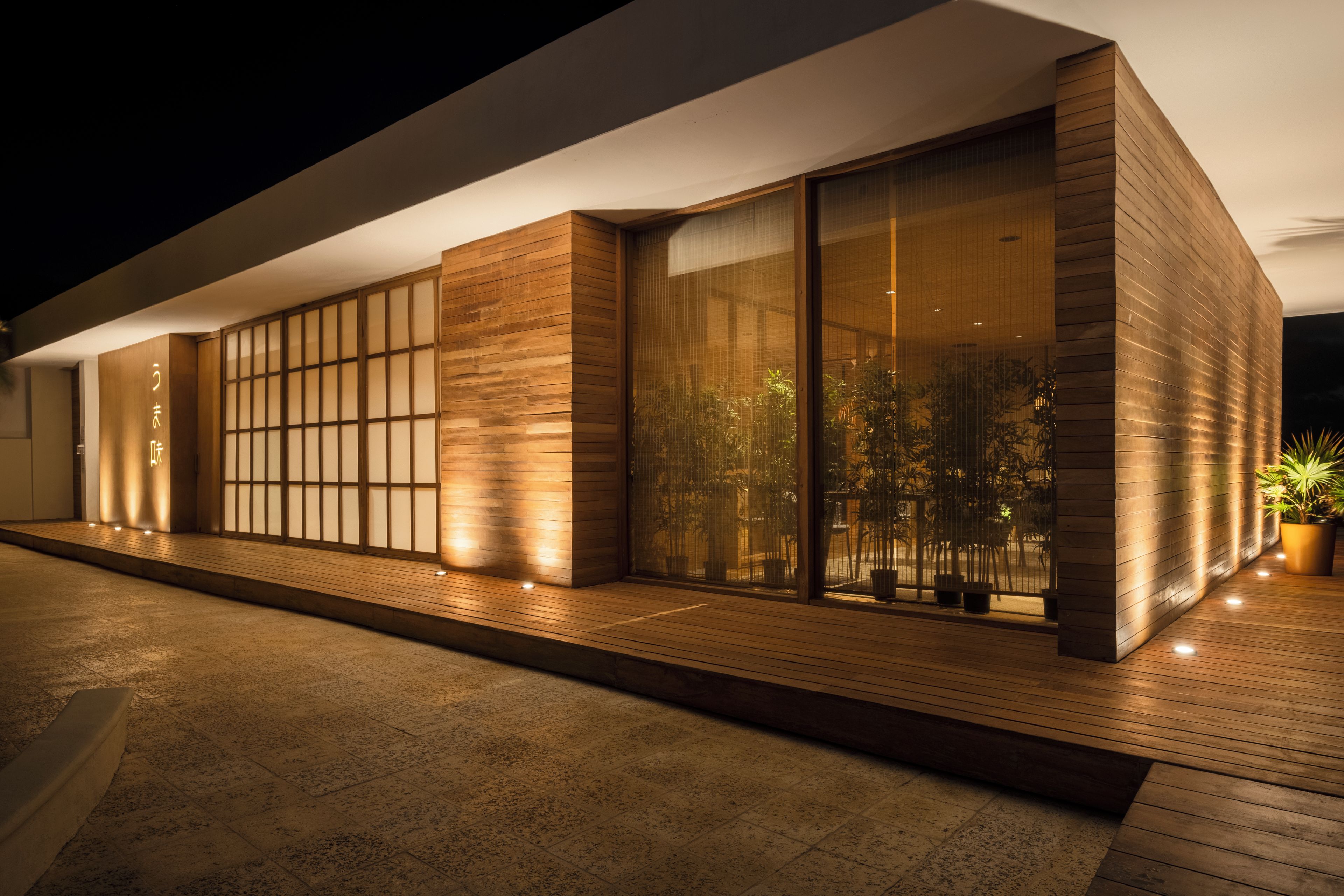 A modern building with large glass windows, wooden paneling, and a paved walkway.