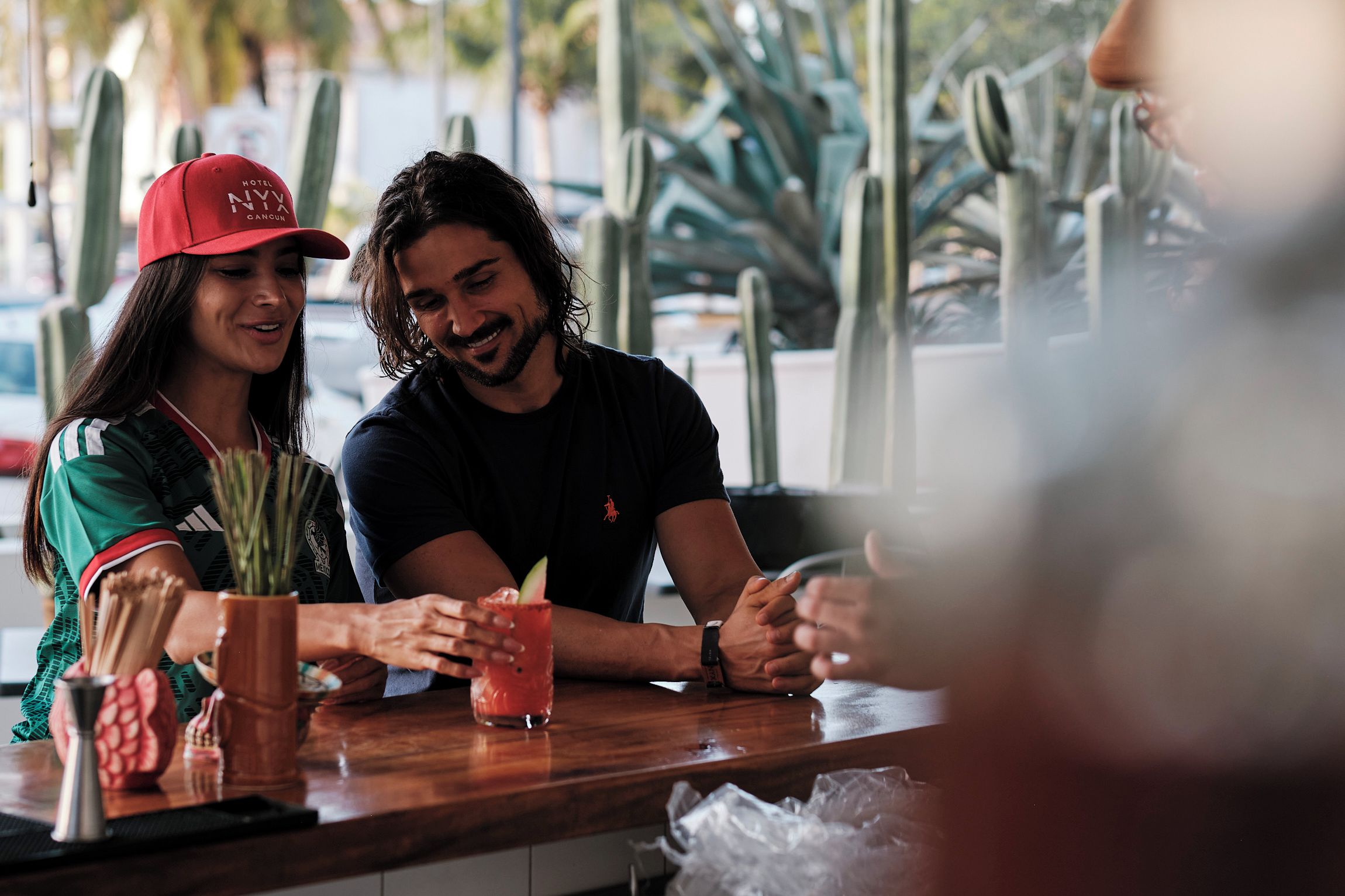 Zona de bar con mostrador de madera, una planta de cactus y una persona con gorra roja.