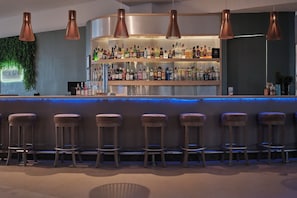 A bar area with a counter, multiple shelves of bottles, and six bar stools. - Hotel NYX Cancun All Inclusive (Cancun)