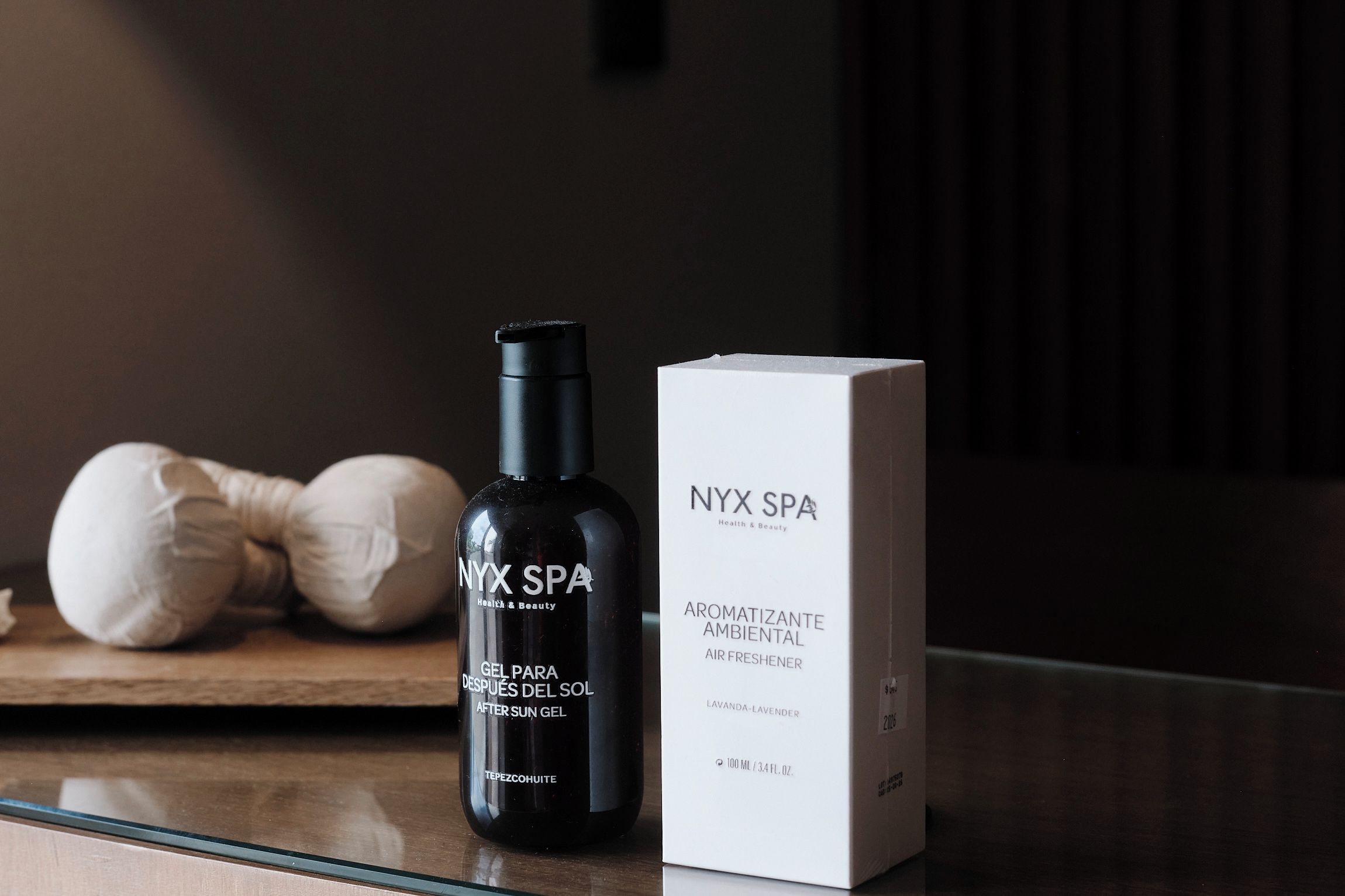 A black bottle and a white box labeled NYX SPA on a reflective surface.