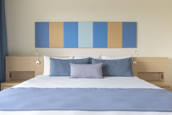 Una cama bien hecha con un edredón azul, cabecera con diseño azul y beige, y lámparas de noche.
