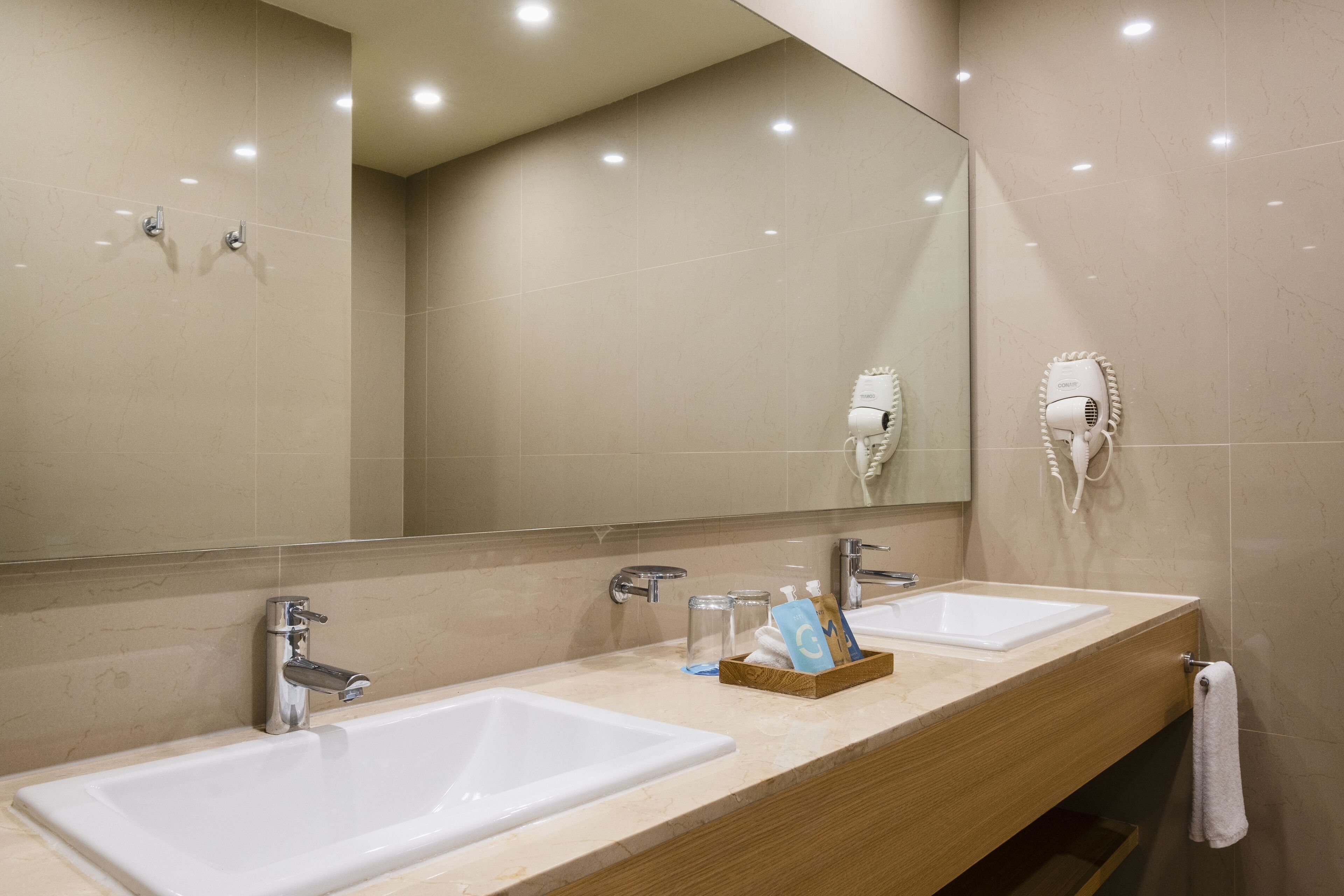 Une salle de bain avec deux lavabos, un miroir et un sèche-cheveux fixé au mur.