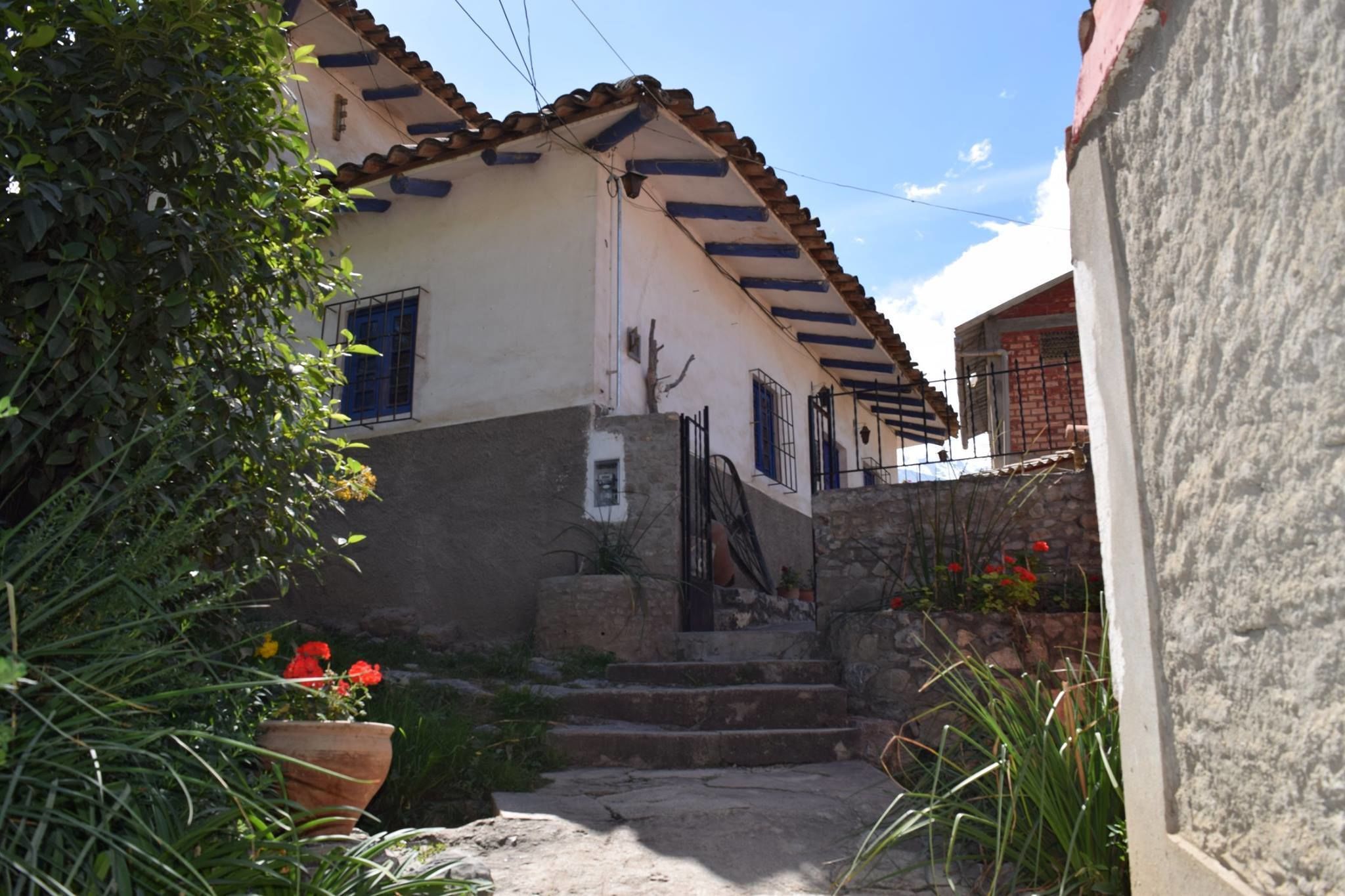 A traditional house with a tiled roof, a staircase leading to the entrance, and a small garden area with potted plants and flowers.