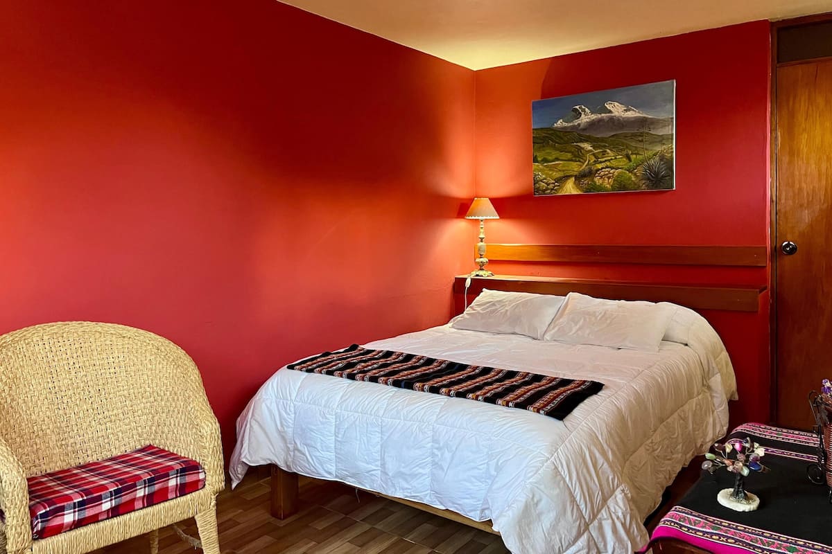 A bedroom with a bed, a chair, a lamp, and a painting on the wall.
