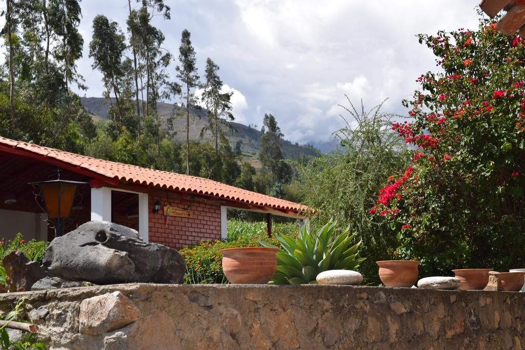 Un edificio rústico con tejado de tejas rojas, rodeado de exuberante vegetación y un telón de montañas.