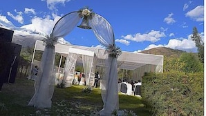 Un lieu de réception pour mariage aménagé sous une tente, avec un ciel dégagé et des montagnes en arrière-plan.