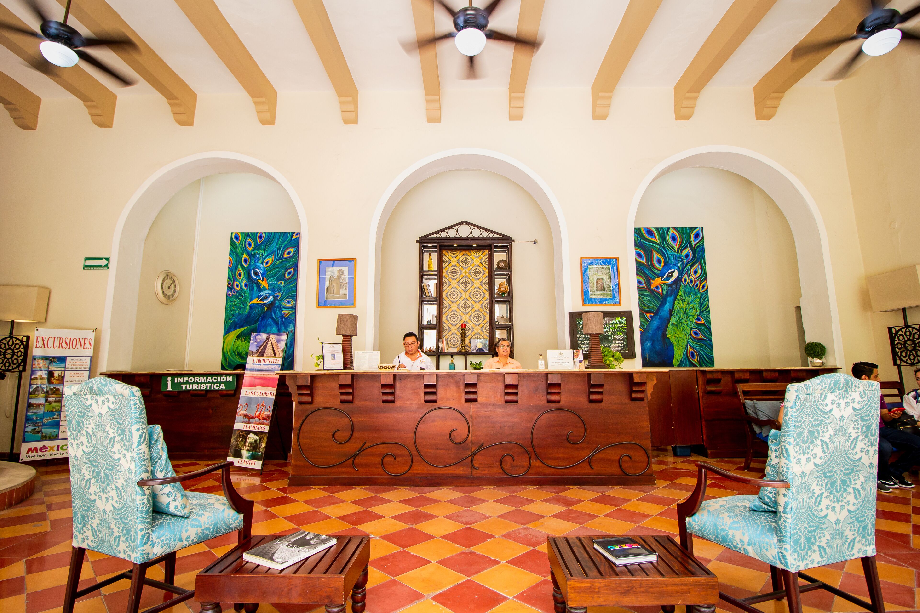 A reception area with a check-in counter, two receptionists, and a decorative peacock painting.