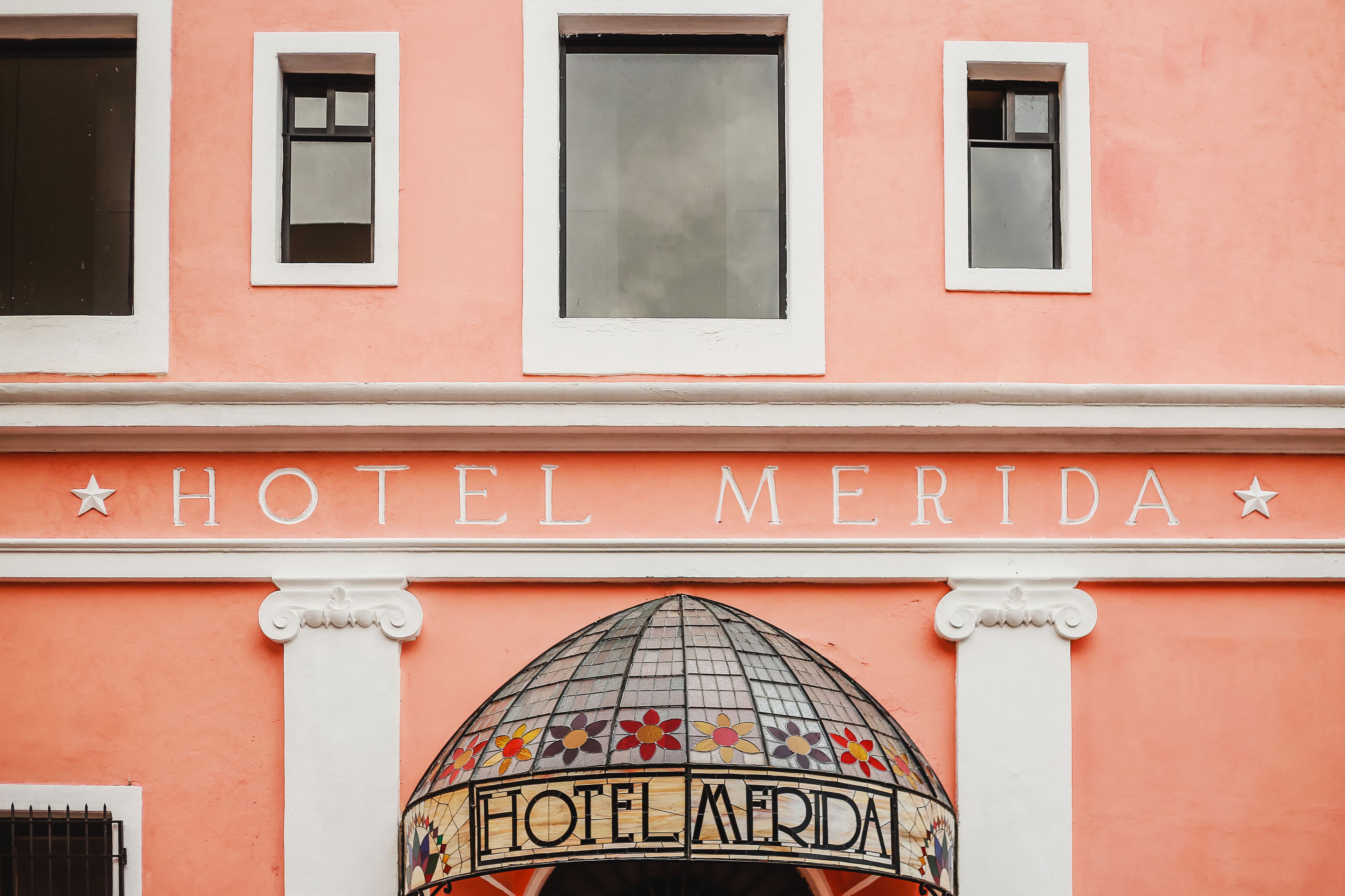 Un bâtiment sur lequel on peut lire l’inscription « HÔTEL MERIDA » au-dessus de l’entrée, et qui est surmonté d’un dôme orné de motifs floraux en mosaïque.