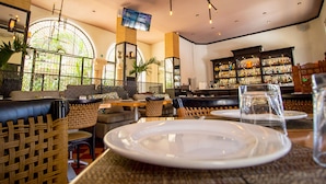 A restaurant with wicker furniture, a bar area with shelves of bottles, and a TV mounted on the wall. - Hotel Merida (Mérida)