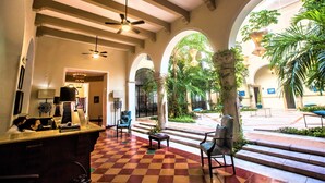 A hotel lobby with a checkered floor, seating areas, a reception desk, and a view of the outdoor courtyard. - Hotel Merida (Mérida)