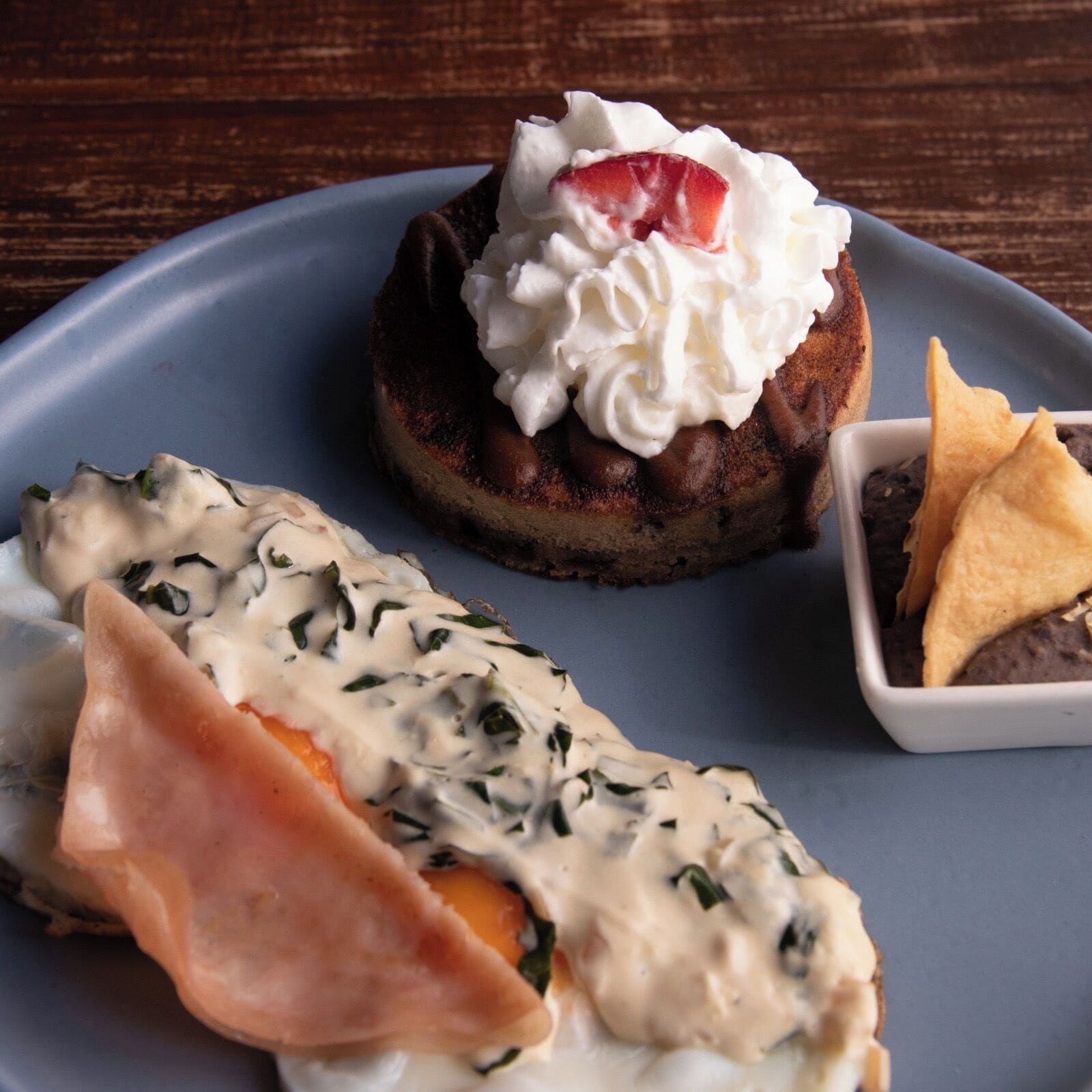 Une assiette avec un dessert garni de crème fouettée et d’une fraise, accompagné d’une part de tarte à la garniture crémeuse et d’une tranche de jambon.