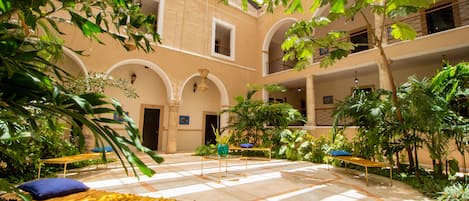 A spacious courtyard with a tiled floor, benches, and lush greenery.