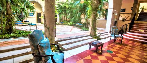 A spacious indoor courtyard with a checkered floor, a staircase, and several chairs with cushions.