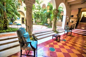 A spacious indoor courtyard with a checkered floor, a staircase, and several chairs with cushions. - Hotel Merida (Mérida)