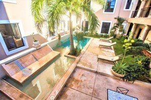 A pool area with a hot tub, lounge chairs, and various plants.