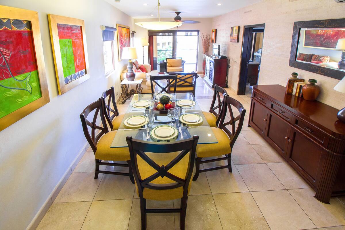 A dining area with a glass table, yellow chairs, and a wooden cabinet.