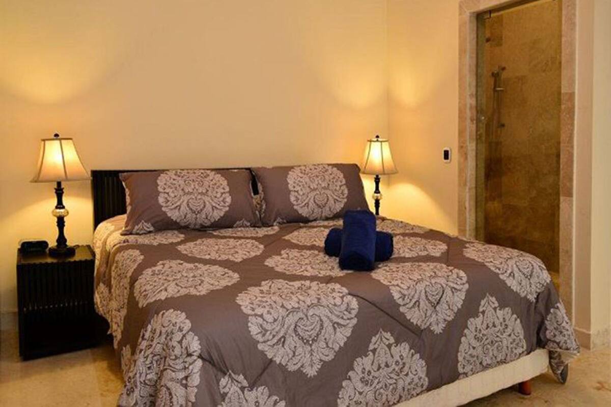 A bedroom with a bed, two bedside lamps, a blue towel, and a door.