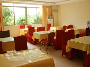Un comedor con mesas y sillas, ventanas amplias con cortinas y un equipo de aire acondicionado.