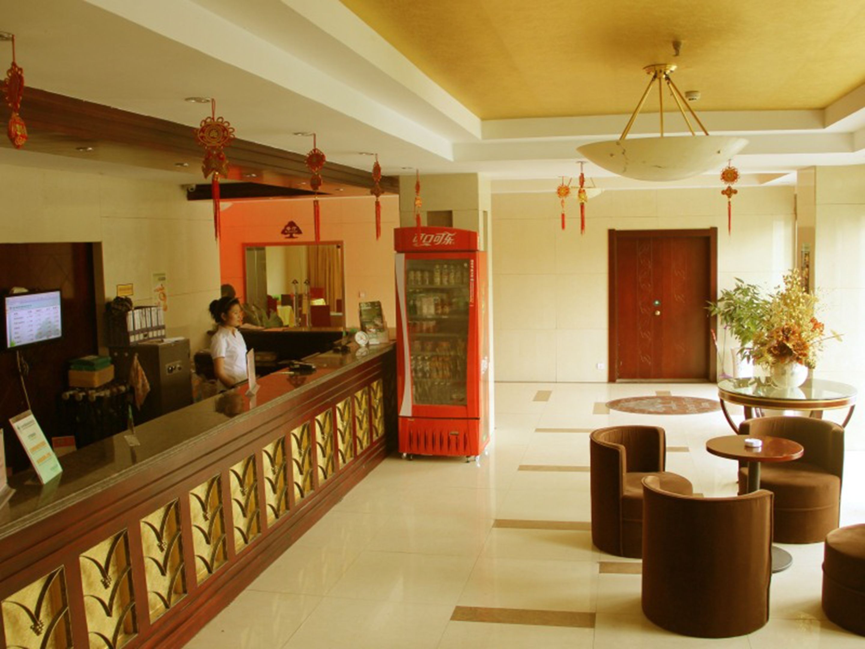 Eine Hotelhalle mit einer Rezeption, einem Coca-Cola-Kühlschrank und einer Sitzecke mit runden Tischen und Stühlen.