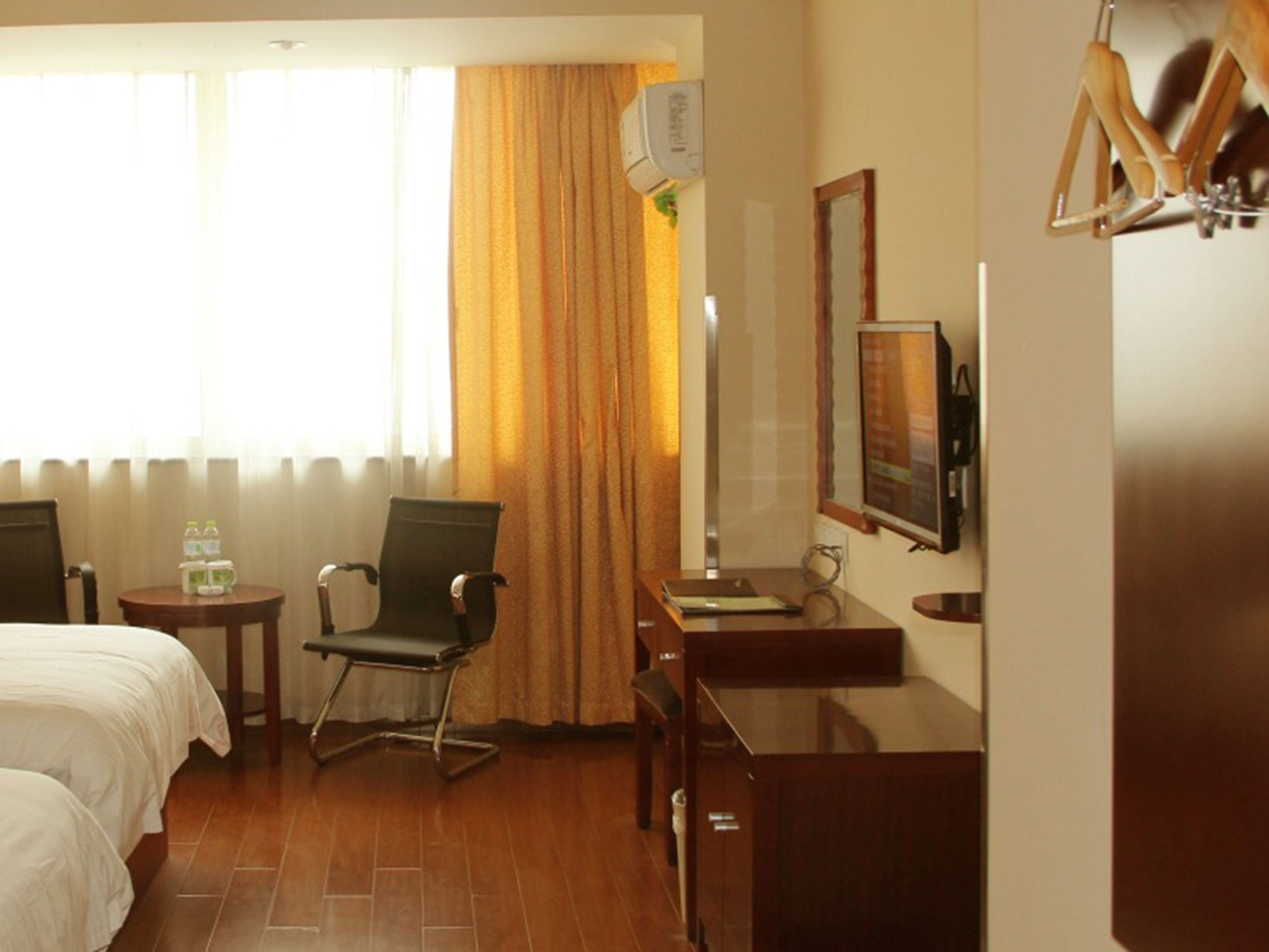 Habitación de hotel con dos camas, un escritorio, una silla, un espejo, una lámpara y una ventana con cortinas.