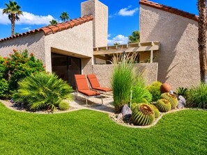Una casa moderna con un patio, dos sillones de descanso y una variedad de cactus y plantas.