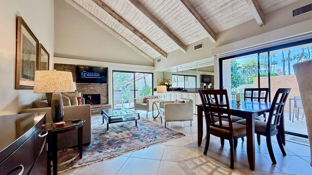 A spacious living area with a fireplace, a television mounted on the wall, and a dining area with a table and chairs.