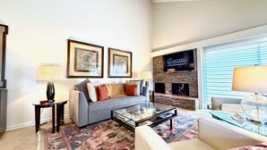 A modern living room with a grey sofa, two framed artworks, a flat-screen TV, and a fireplace.