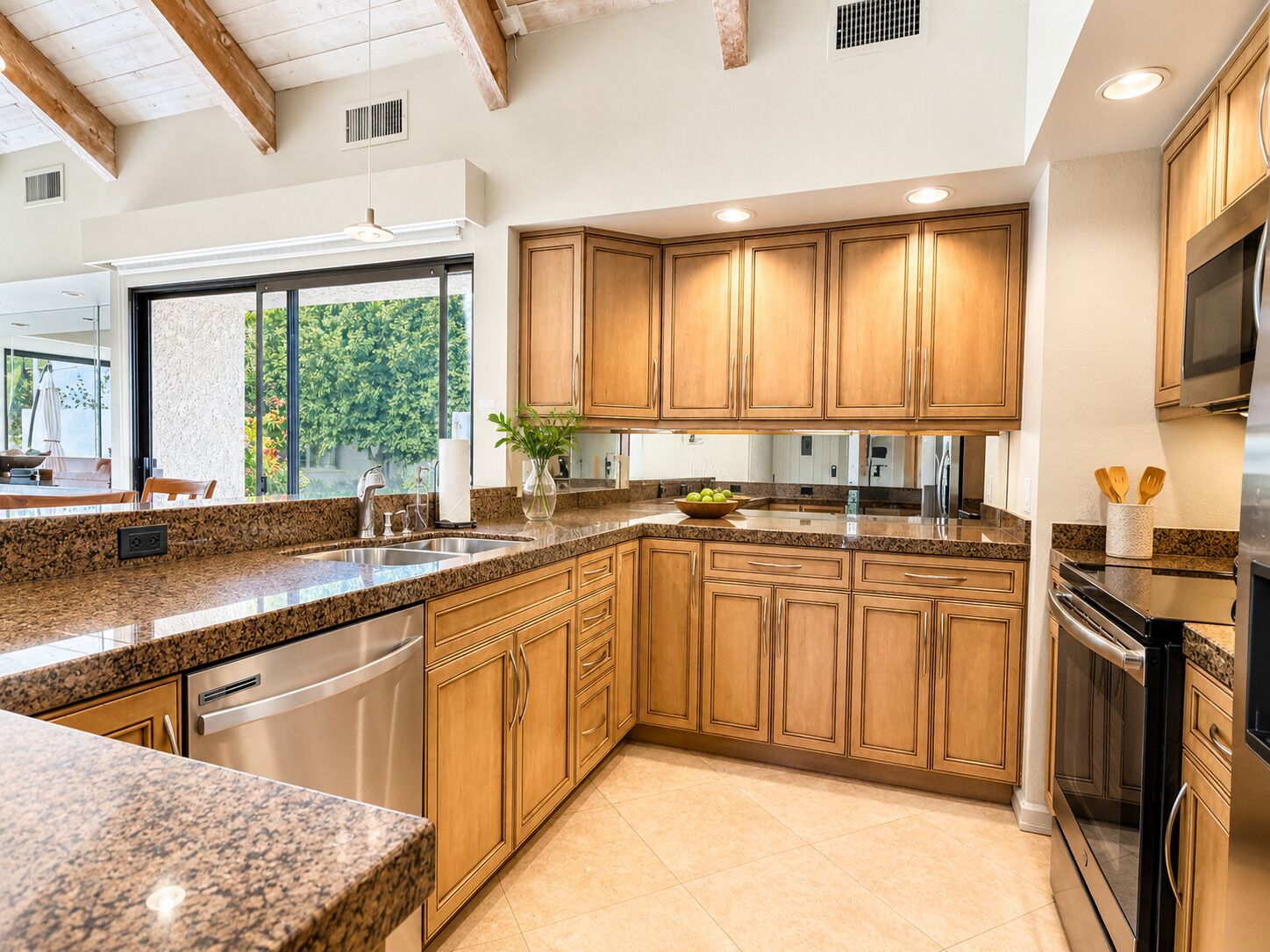 Cocina con encimeras de granito, armarios de madera, electrodomésticos de acero inoxidable y un amplio ventanal con vistas al verdor.