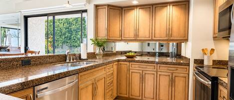 Cocina con encimeras de granito, armarios de madera, electrodomésticos de acero inoxidable y un amplio ventanal con vistas al verdor.