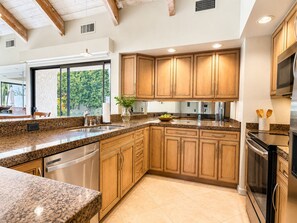 Cocina con encimeras de granito, armarios de madera, electrodomésticos de acero inoxidable y un amplio ventanal con vistas al verdor.