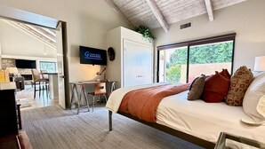 A modern bedroom with a large bed, a desk, and a TV mounted on the wall.