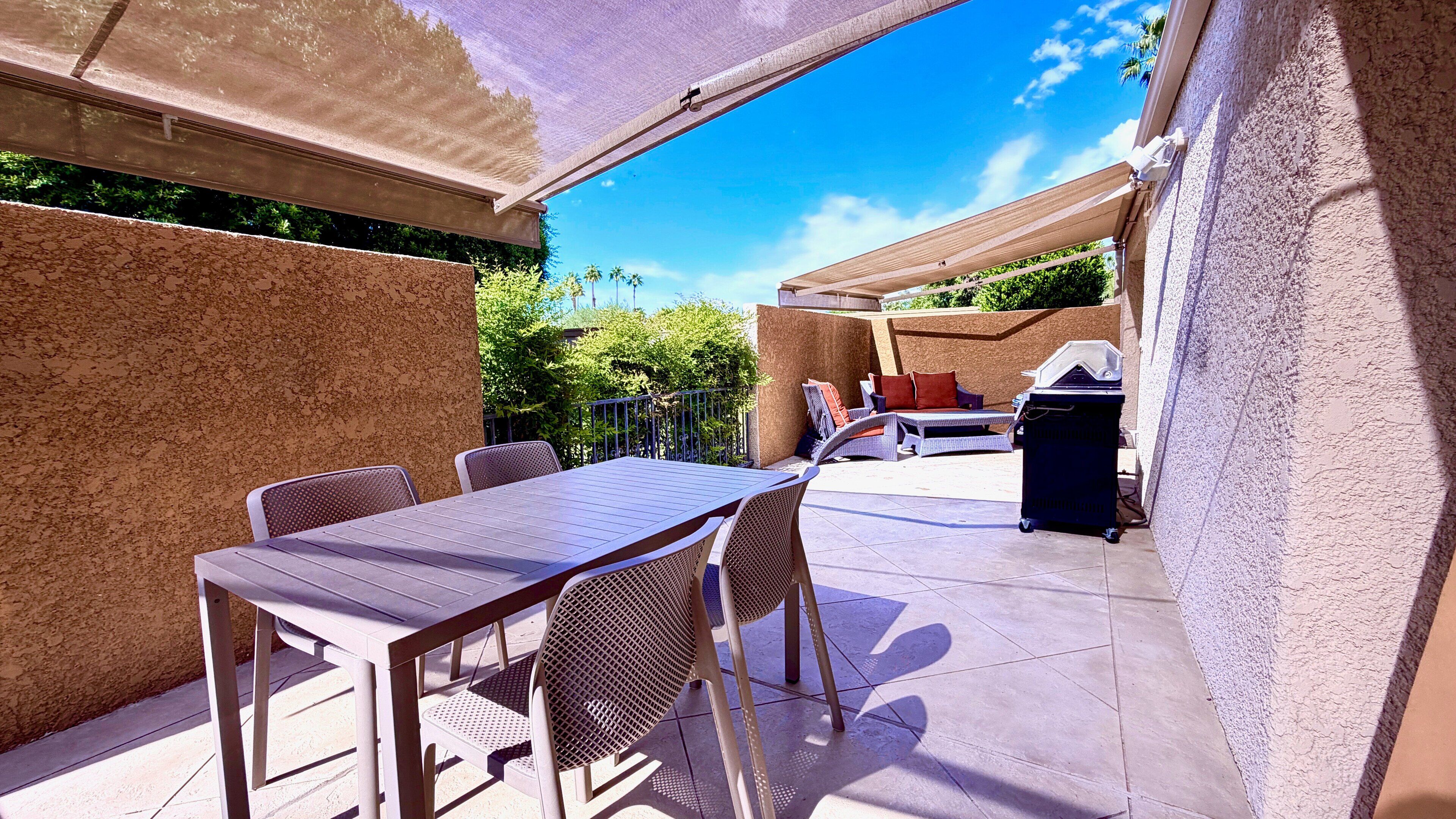 An outdoor patio with a table and chairs, a grill, and a covered seating area.
