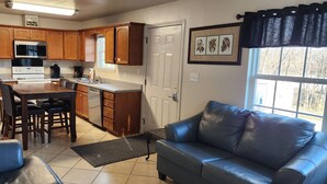 A compact kitchen with wooden cabinets, a refrigerator, microwave, and a dining area with a table and chairs. - Experience Comfort and Convenience in the Heart of Knoxville (Knoxville)