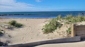 Une plage de sable avec une promenade en bois menant à l’eau, un ciel dégagé et une mer calme.