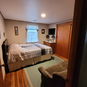Une chambre à coucher comprenant un lit, une table de chevet, un téléviseur, une armoire en bois et une fenêtre avec des rideaux.