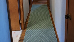 A narrow hallway with wooden doors, a green patterned rug, a small table with a pitcher, and a mirror on the wall. - Great Vacation Place Just Steps From The Beach (Falmouth)