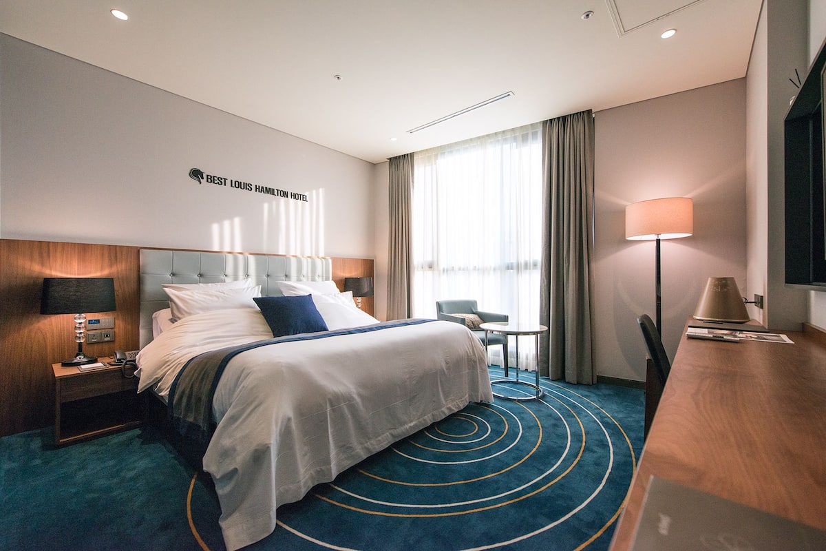 A hotel room with a large bed, a desk, a chair, and a TV.