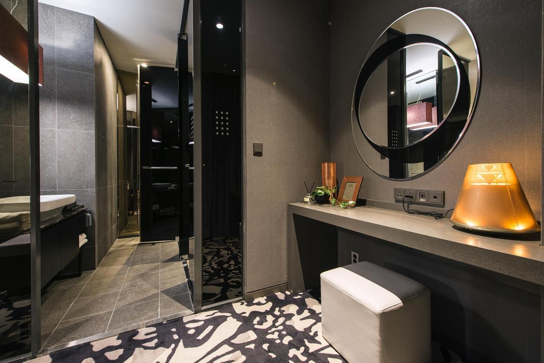 A modern bathroom with a vanity, a mirror, a toilet, and a patterned rug.