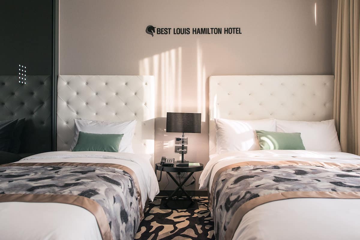 A hotel room with two beds, a headboard with a logo, a lamp, and a patterned carpet.