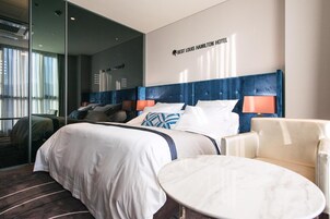 Una habitación de hotel con una cama grande, una mesa redonda y una silla. Se observa una pared con un cartel que dice "Best Louis Hamilton Hotel".