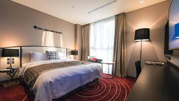 A hotel room with a large bed, a desk, a chair, a TV, and a window with curtains.