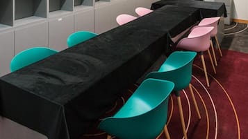 Una sala de conferencias con una larga mesa, sillas color turquesa y un televisor en la pared.